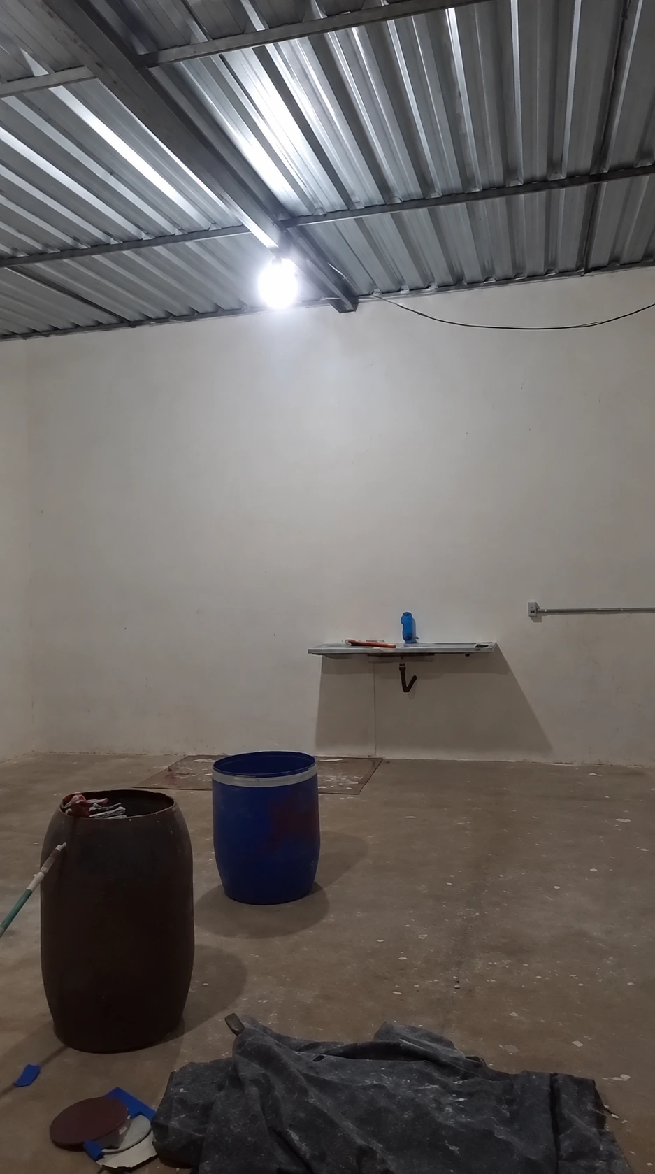 Ambiente interno com paredes claras, cobertura metálica e recipientes no piso